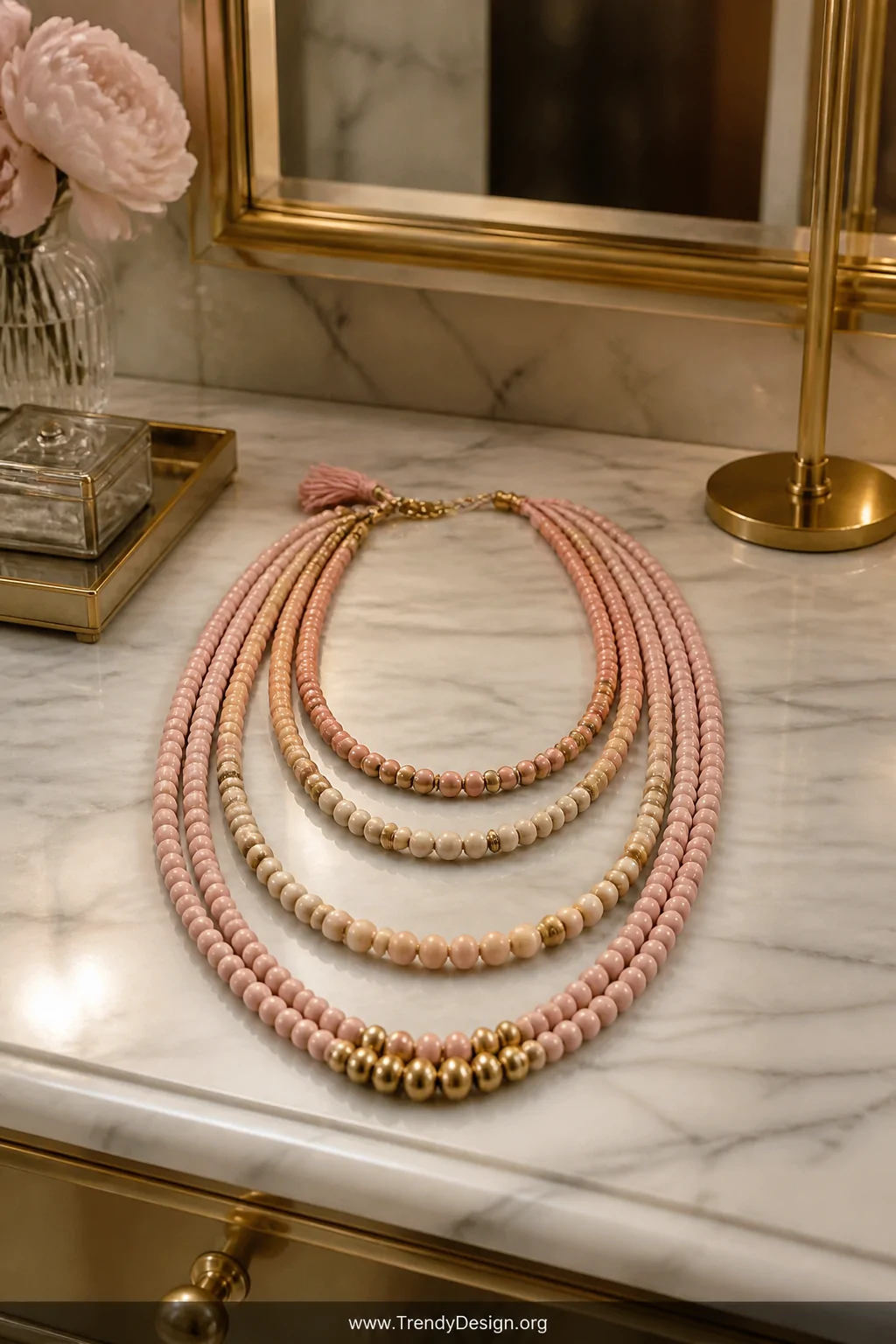 A wide styled shot on a marble and brass vanity surface showing three layered multi-strand pony bead necklaces of cascading l