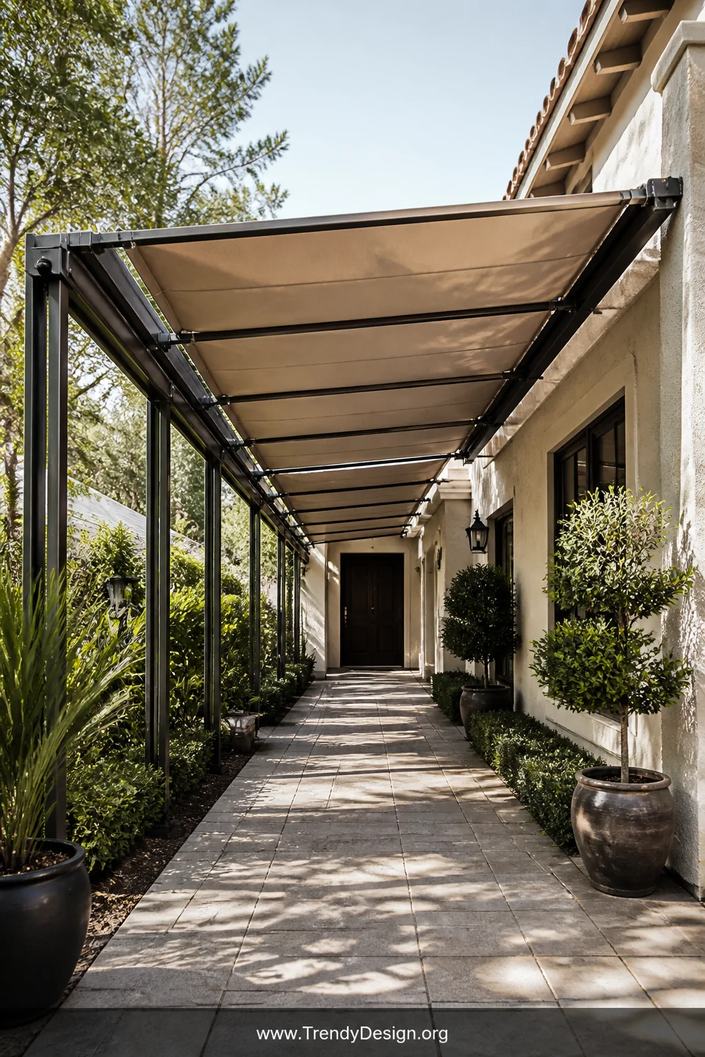 A wide shot of a retractable fabric walkway canopy system partially extended over a front path, featuring sand-toned Sunbrell
