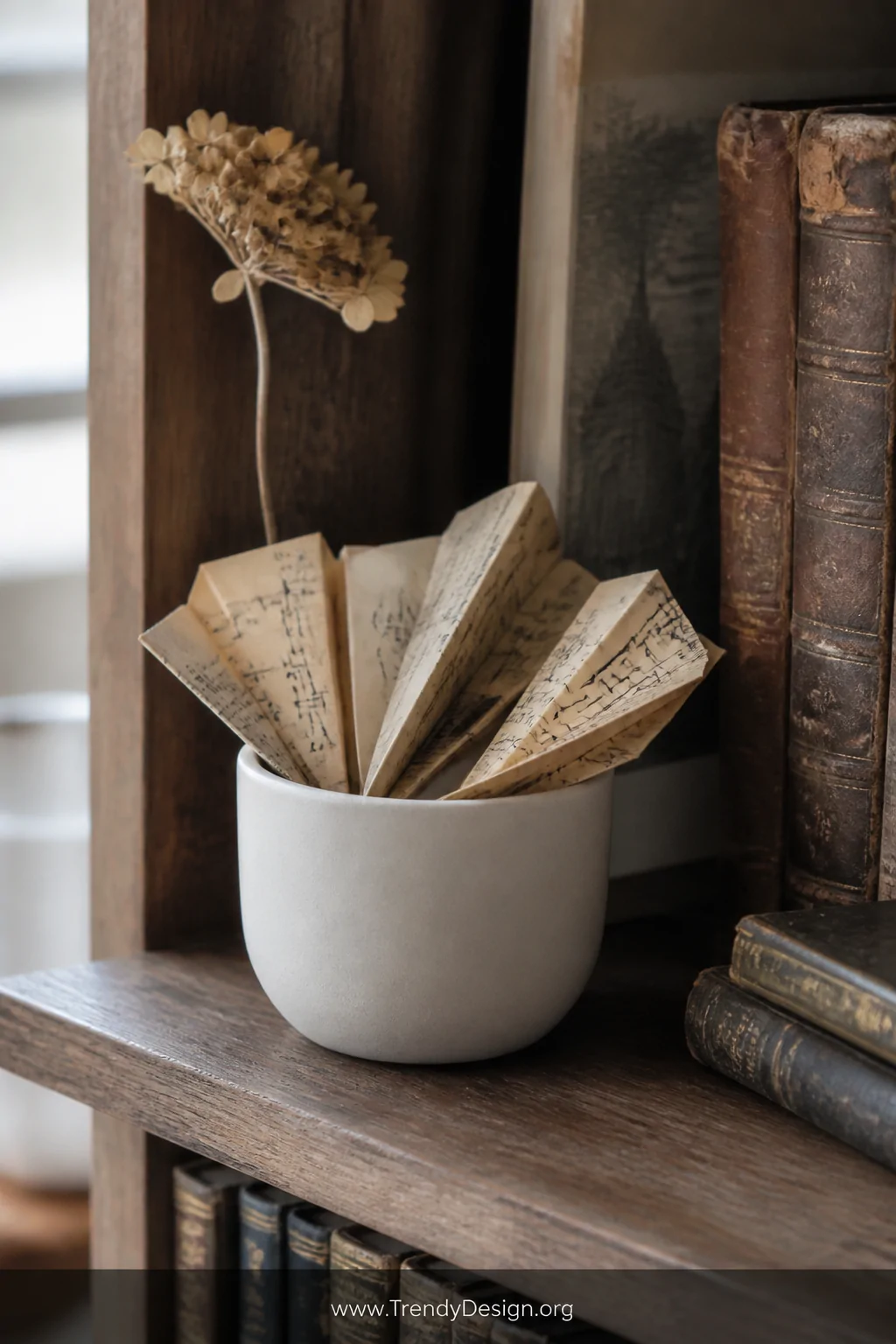 Closeup detail shot of a rustic wooden bookshelf styled with a small matte white ceramic pot holding a fan of mini paper airp