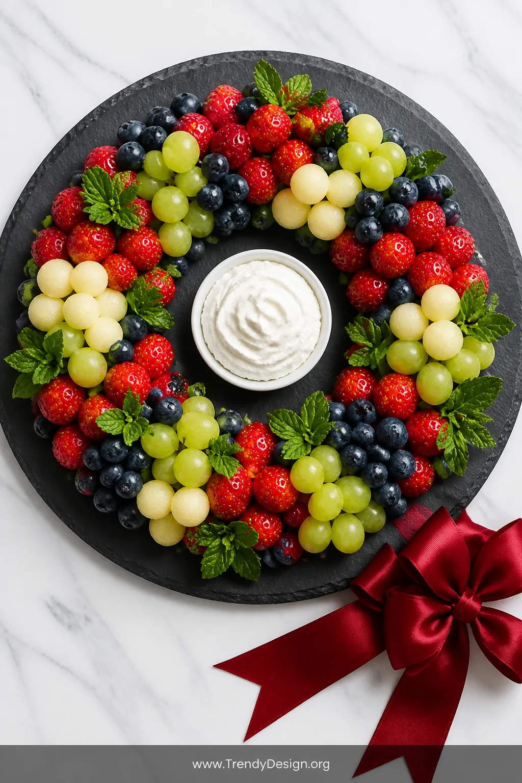 A straight-down overhead flat lay shot of a circular wreath-shaped fruit arrangement on a large round dark slate board, lush 