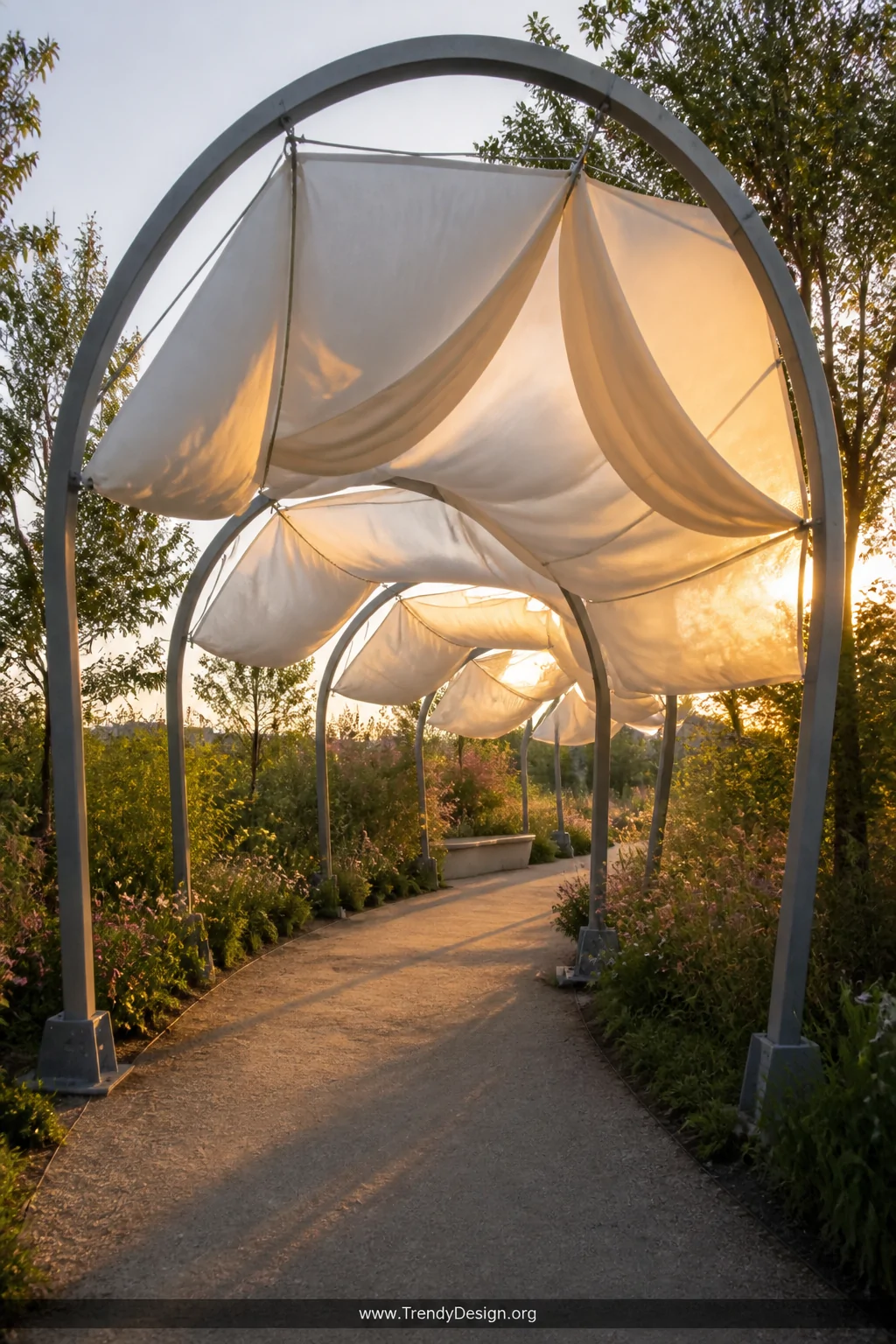 A wide romantic exterior shot of a curved arched steel frame canopy walkway draped in flowing white and cream fabric panels, 