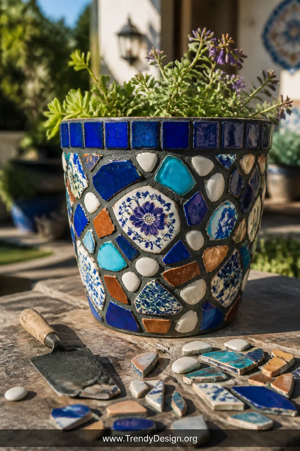 A detail shot of a mosaic-decorated plastic plant pot encrusted in fragments of cobalt blue and terracotta broken china, vivi