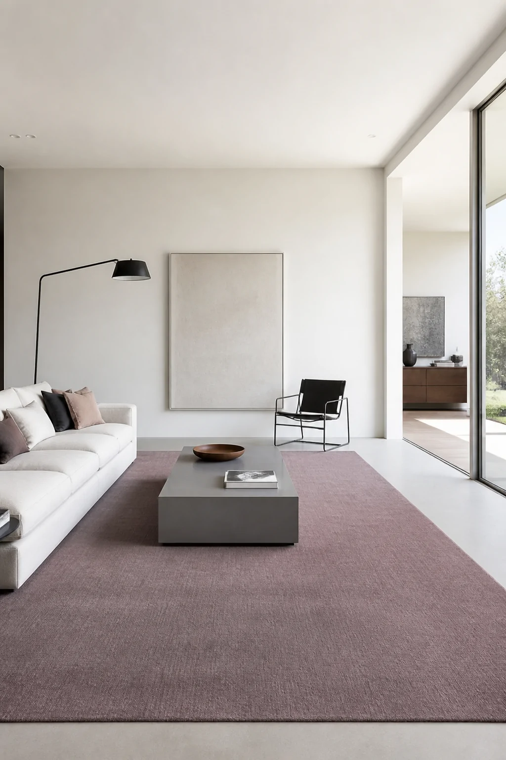 Wide room shot of a sleek minimalist living room with a large solid dusty mauve low-pile rectangular rug covering most of the