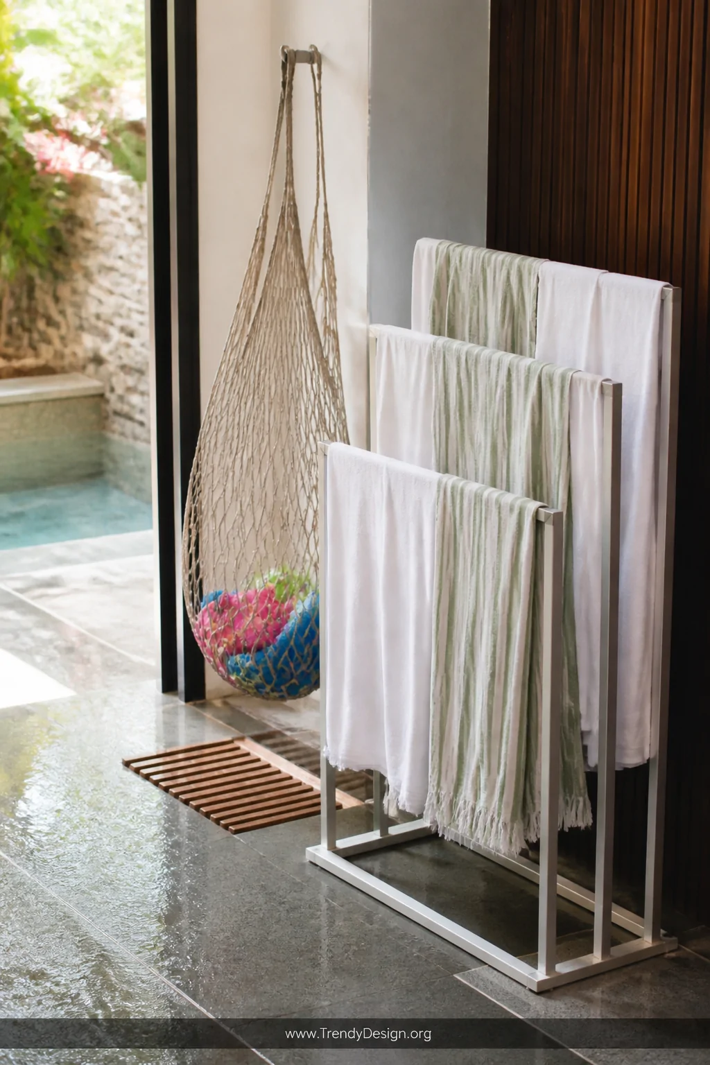 Medium shot of a freestanding brushed aluminum towel drying rack positioned near a pool exit on wet slate tile, draped with w