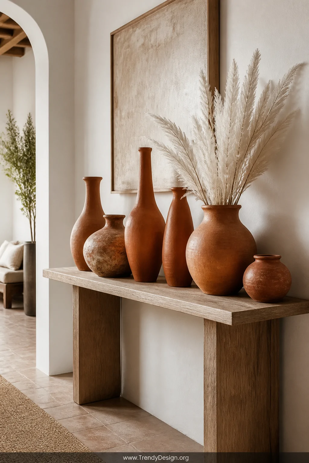 A wide shot of a styled entryway console table in natural oak holding an artful grouping of terracotta clay vases in varying 