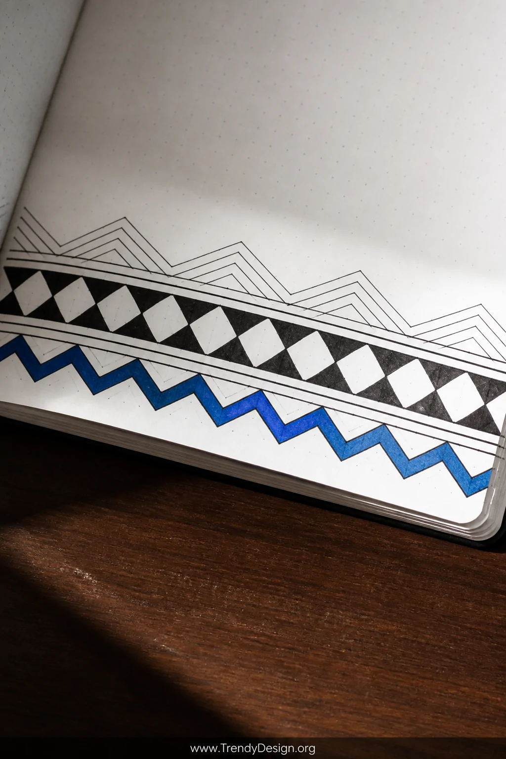 A closeup detail shot of a bullet journal page on a dark walnut desk surface, showing a precisely ruled geometric divider ban