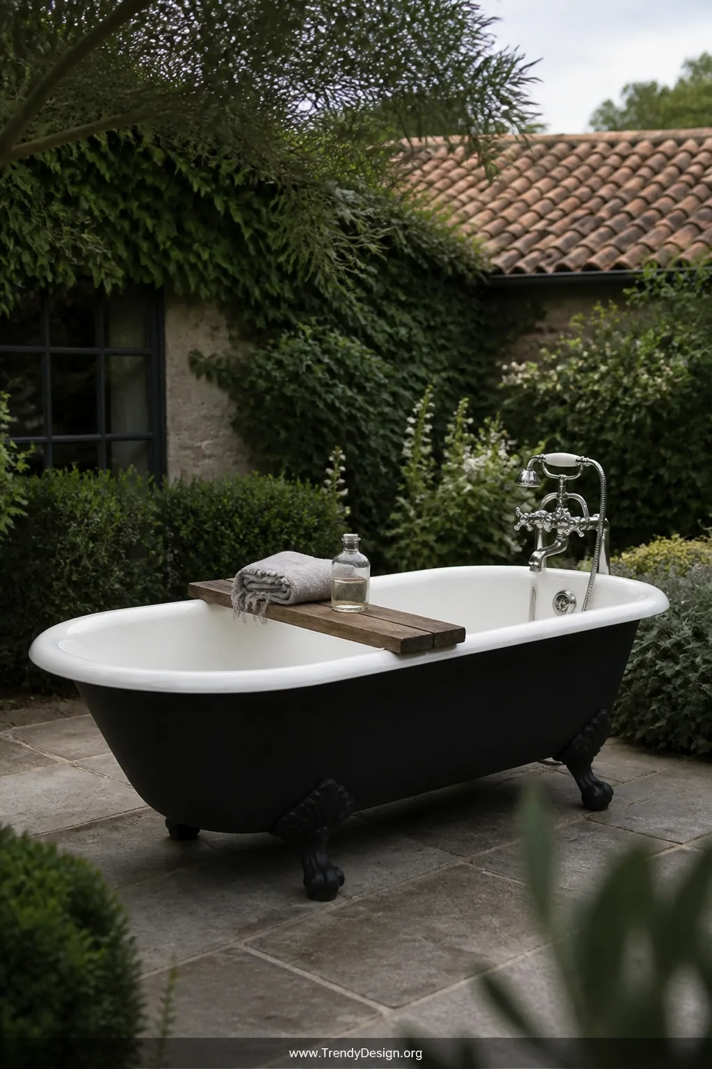 Medium outdoor garden shot of a vintage white cast iron clawfoot bathtub with a freshly painted matte black exterior sitting 