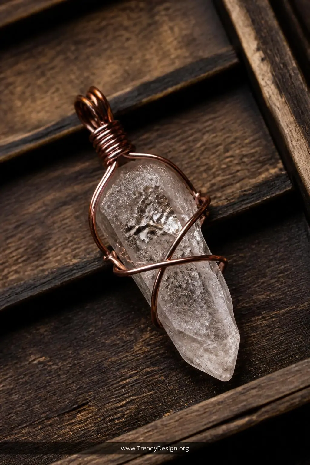 Raw crystal quartz point wrapped in copper wire on a weathered wooden jewelry display tray, warm amber studio lighting, closeup of the wire cage bail and irregular stone texture against dark wood grain