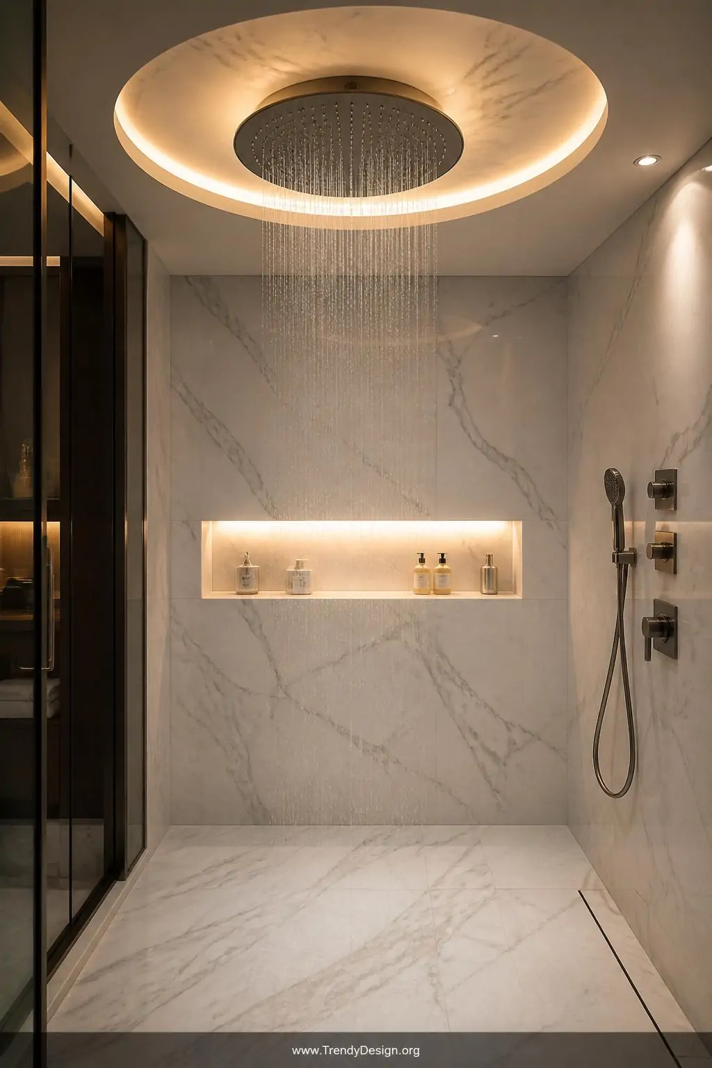 Large circular rainfall showerhead mounted flush to a marble-inset recessed ceiling niche glowing with warm LED strip lighting in a luxury walk-in shower, hotel-spa style, cool white marble tiles contrasting with a softly illuminated built-in shelf holding minimal glass bottles, wide shot, photorealistic interior design.