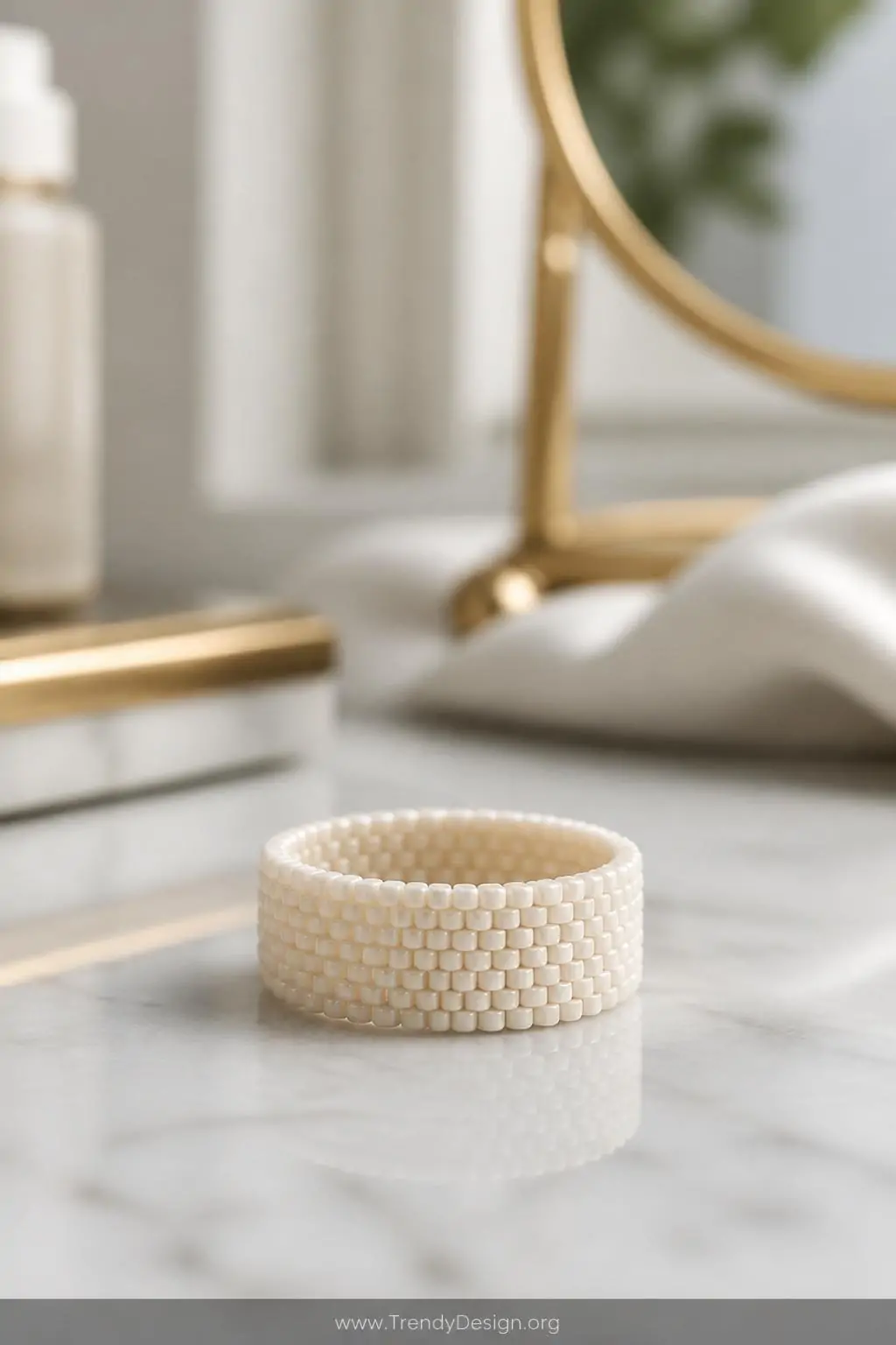 Flat seed bead band ring in monochromatic ivory with Miyuki Delica cylinder beads on a polished white marble vanity surface, soft diffused natural window light, extreme closeup showing even peyote stitch texture and refined glossy finish