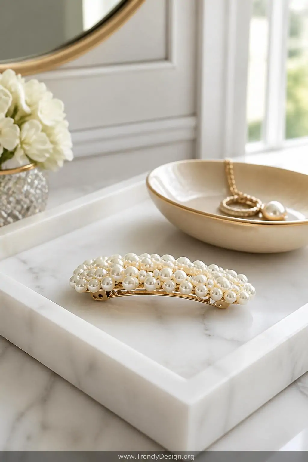 Creamy white pearl beaded barrette resting on a white marble vanity tray beside a champagne-toned jewelry dish, soft diffused natural window light, elegant minimalist dressing room, closeup shot.