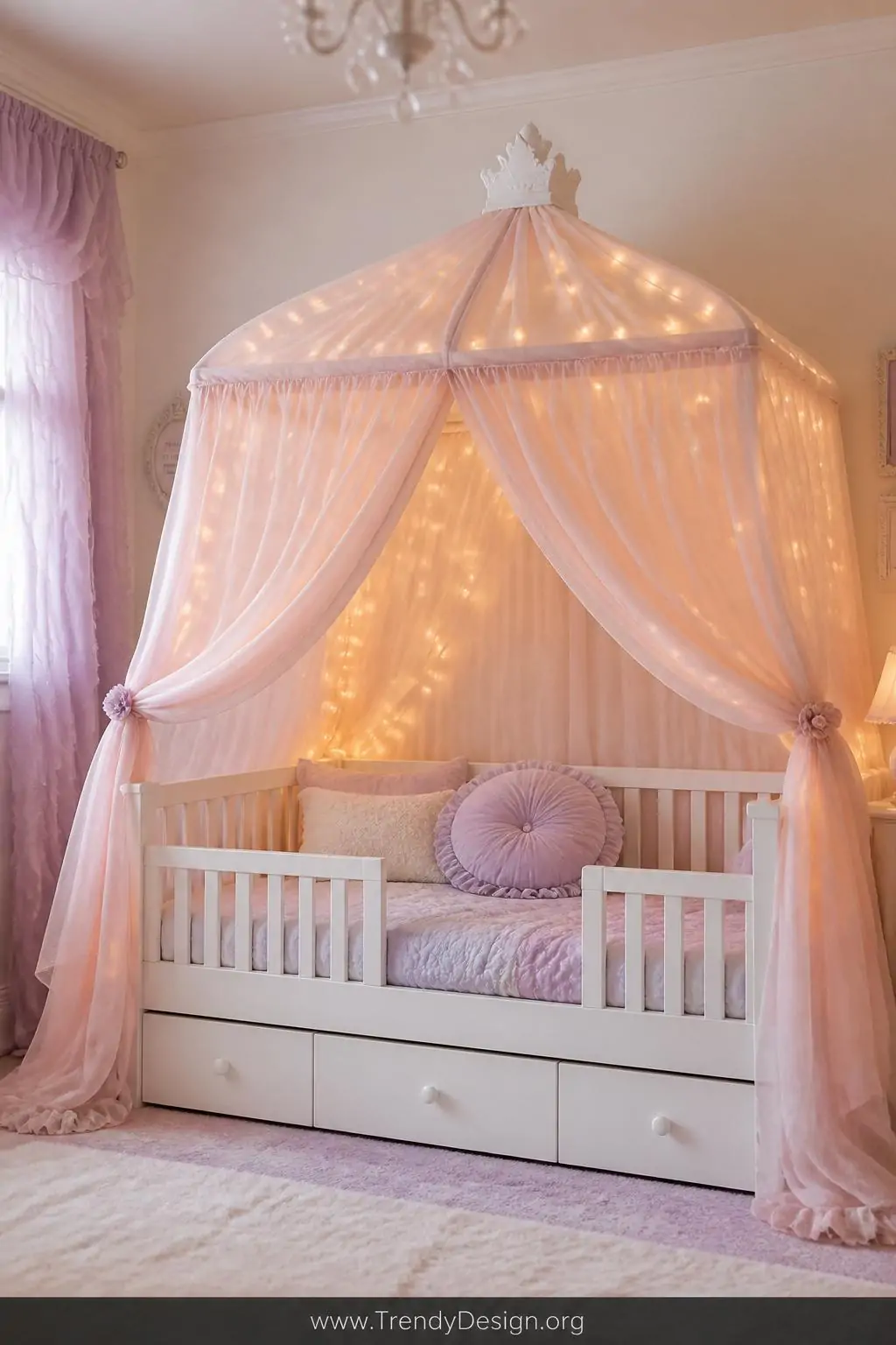 White canopy toddler bed draped in sheer blush pink fabric with delicate string lights glowing inside the canopy, in a soft pastel girl's bedroom, fairytale nursery style, lavender and cream bedding with a ruffled pillow, warm golden light filtering through gauze, wide shot showing safety rails and full canopy silhouette against a pale wall, photorealistic interior design.