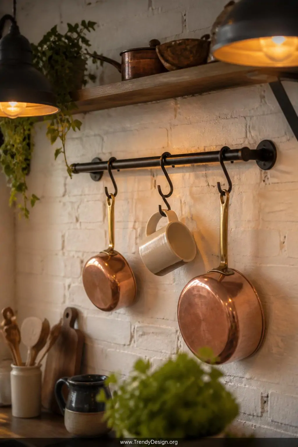 Set of three dark iron S-hooks hanging from a matte black kitchen rail mounted on a whitewashed brick wall, beeswax-finished mild steel catching warm amber pendant light above a display of copper pots and ceramic mugs, medium shot.
