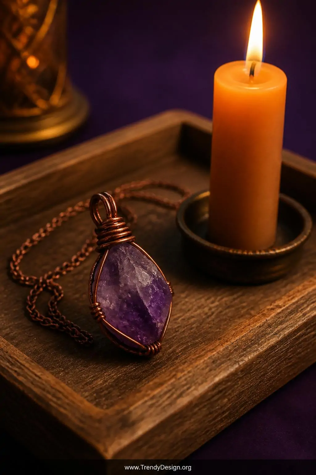 Raw amethyst crystal pendant wrapped in coiled copper wire resting on a weathered wooden jewelry tray beside a single lit taper candle, warm amber glow, rich purple and burnt orange tones, closeup macro shot