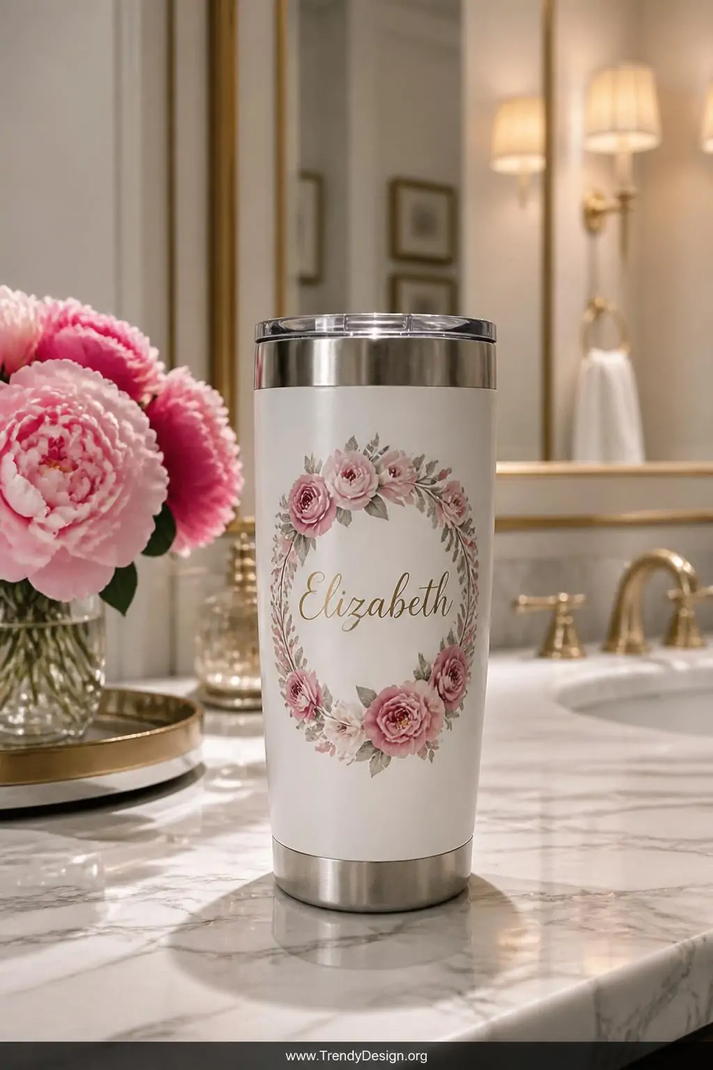 A wide shot of a sleek 20oz stainless steel tumbler displayed on a white marble vanity surface, featuring an elegant cursive 