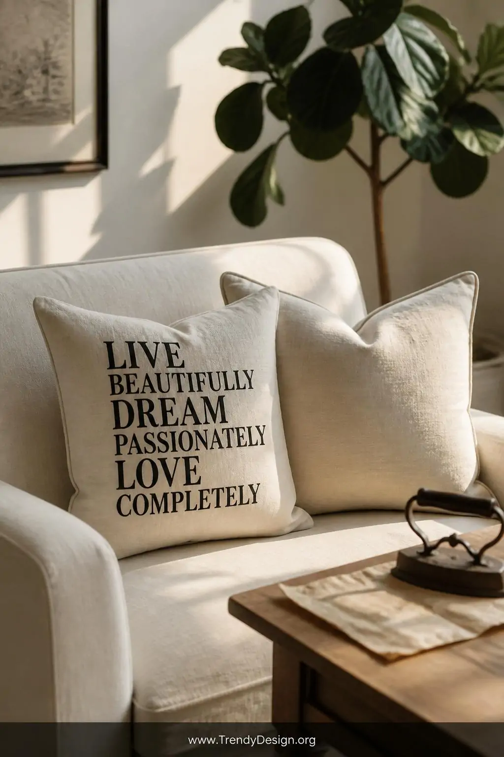 A sunlit living room corner featuring two plump linen throw pillows on a cream linen sofa, one displaying a bold black serif 