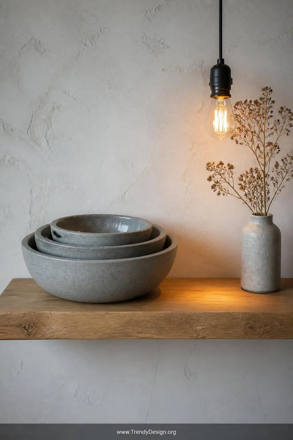 Three perfectly spherical smooth concrete bowls in graduating sizes are nested together on a raw oak floating shelf against a