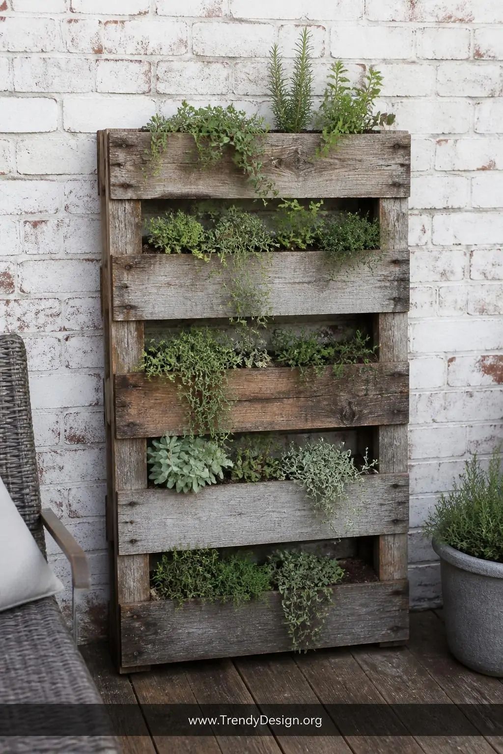 Reclaimed pallet wood vertical planter standing upright against a whitewashed brick wall on a rustic outdoor patio, weathered grey and brown wood tones with trailing succulents and herbs spilling through the uneven slats, medium shot capturing the raw imperfect character of the aged wood texture, soft diffused natural daylight, photorealistic interior design.