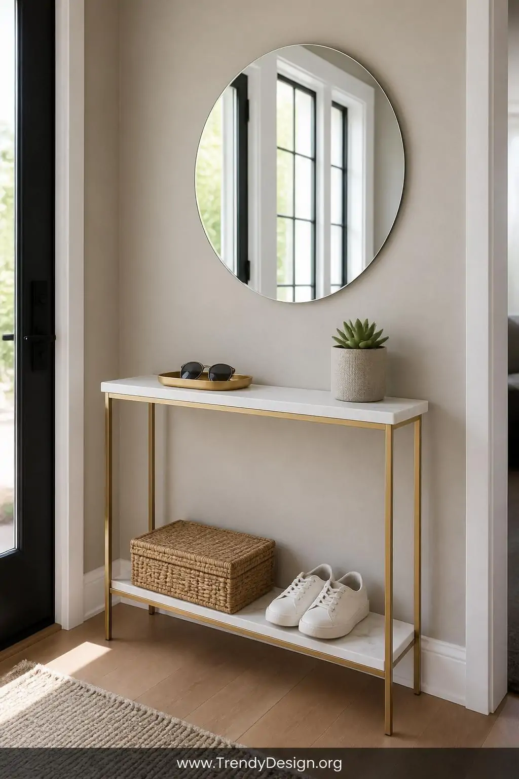 Slim white marble-topped console table under 12 inches deep positioned against a soft greige entryway wall, styled with a brushed gold catchall tray holding folded sunglasses and a small succulent, a round frameless mirror above bouncing natural light, and a neatly folded wicker basket tucked on the lower shelf beside a pair of white sneakers, wide shot, photorealistic interior design.
