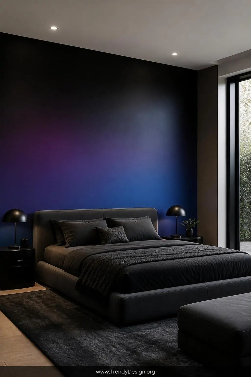 Full bedroom accent wall painted in seamless gradient black-to-deep-purple-to-cobalt wash behind a low-profile upholstered bed with charcoal bedding, matte paint absorbing soft recessed ceiling light for dimensional depth, wide shot.