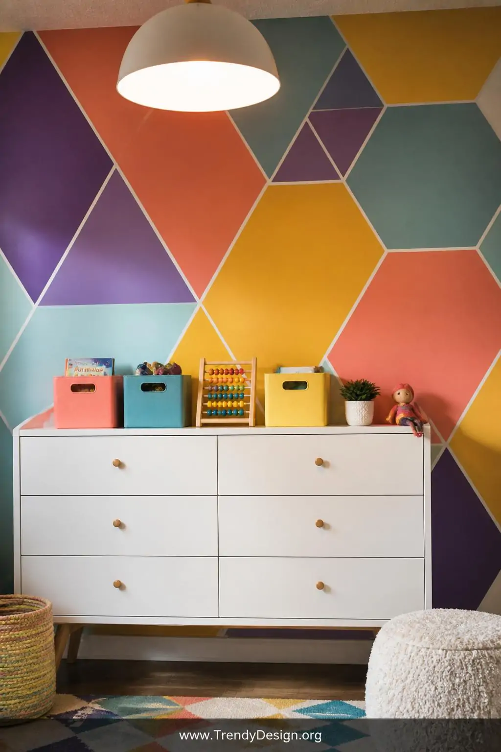 Bold peel-and-stick geometric accent wall of oversized rainbow triangles and hexagons in coral, golden yellow, teal, and violet behind a white mid-century kids dresser topped with colorful toy bins, medium shot, bright overhead pendant light casting clean shadows across the layered pattern, photorealistic interior design.