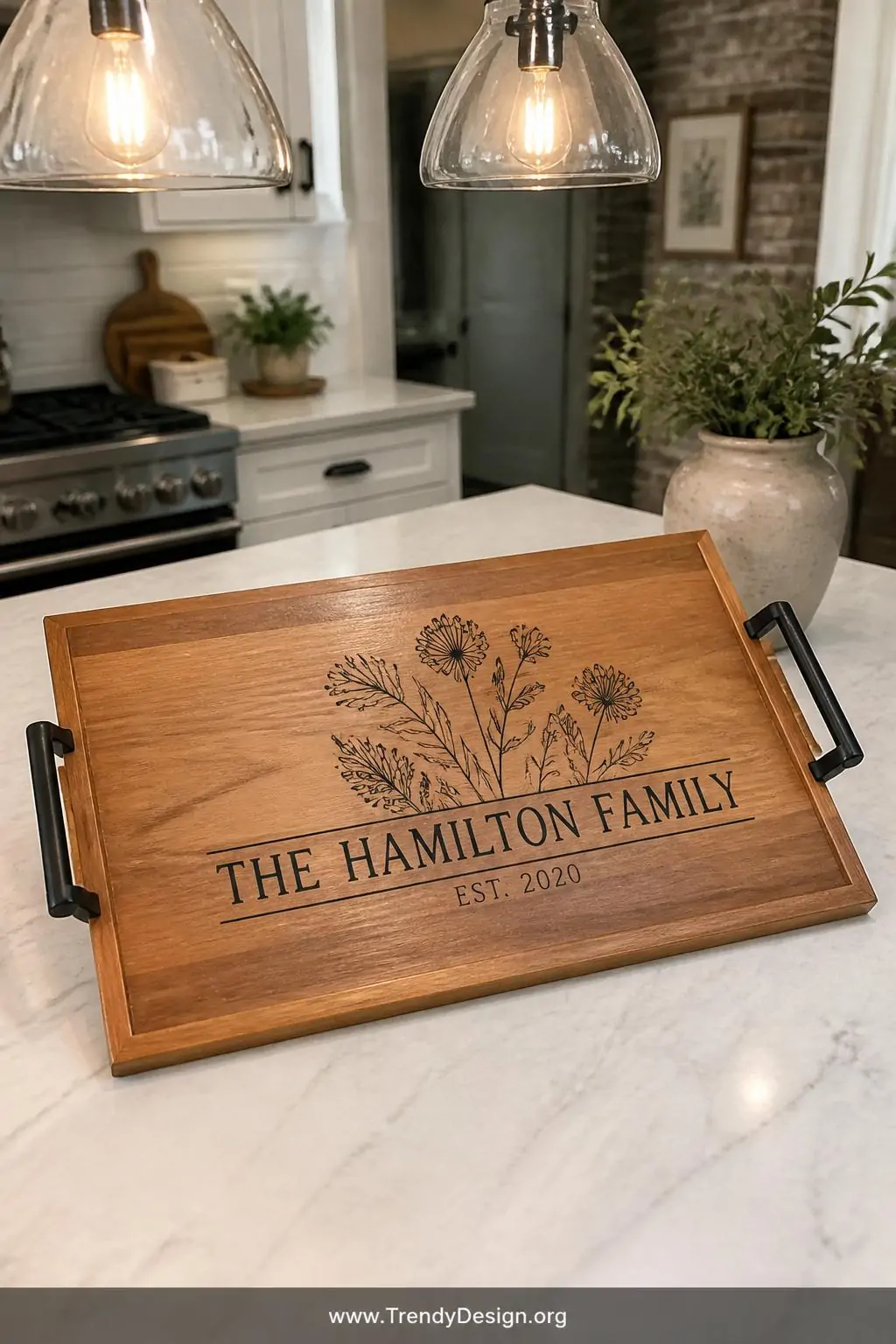 Smooth wooden serving tray with pressed botanical illustration and family name in black vinyl on a marble kitchen island, farmhouse style, soft overhead pendant lighting, closeup showing wood grain texture beneath the crisp geometric vinyl design.