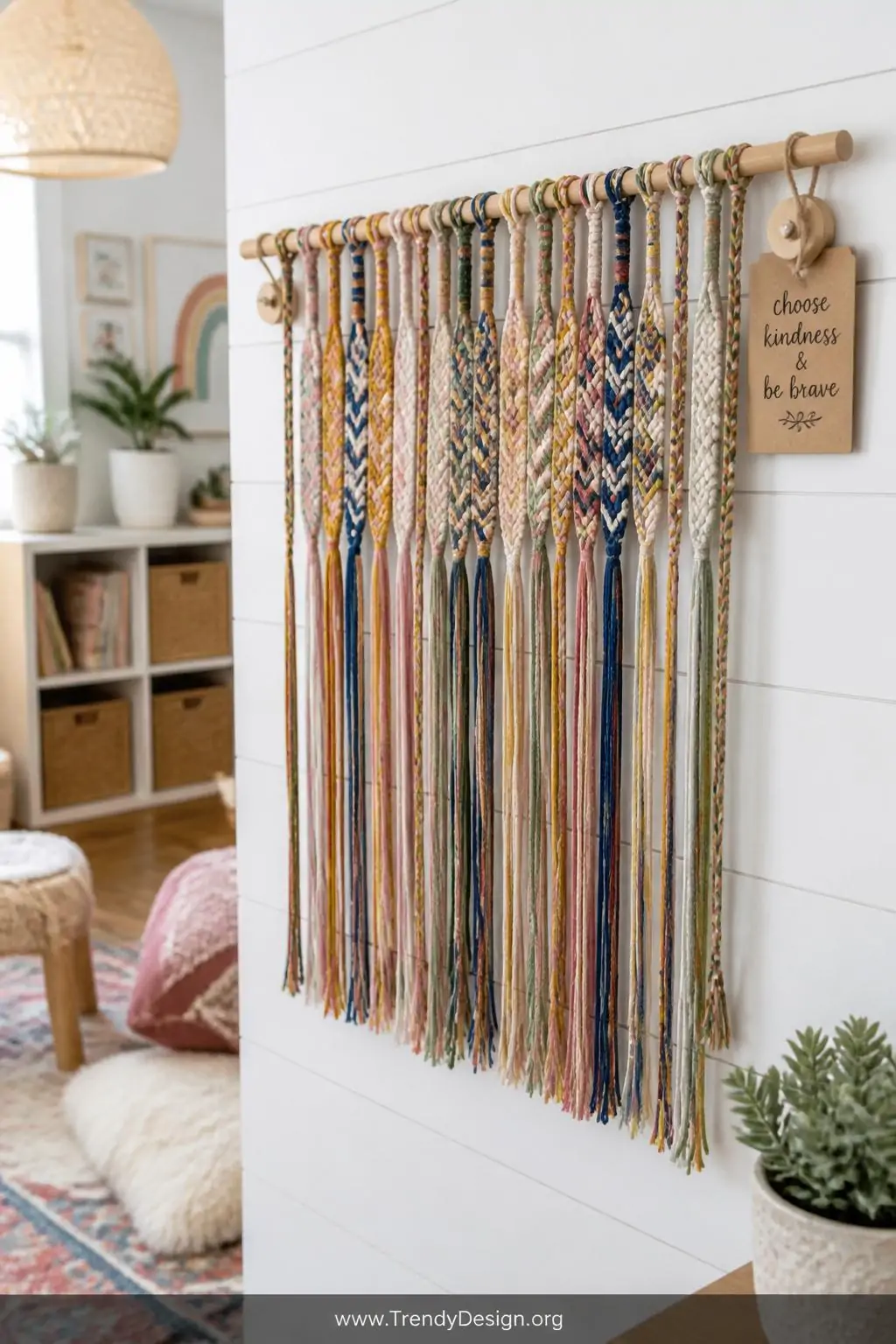Colorful embroidery floss friendship bracelets in chevron and braid patterns tied along a natural wooden dowel mounted on a white shiplap wall in a boho playroom, threads in mustard, blush, cobalt, and sage cascading down with a small hand-lettered kraft paper tag, soft diffused afternoon light, medium shot