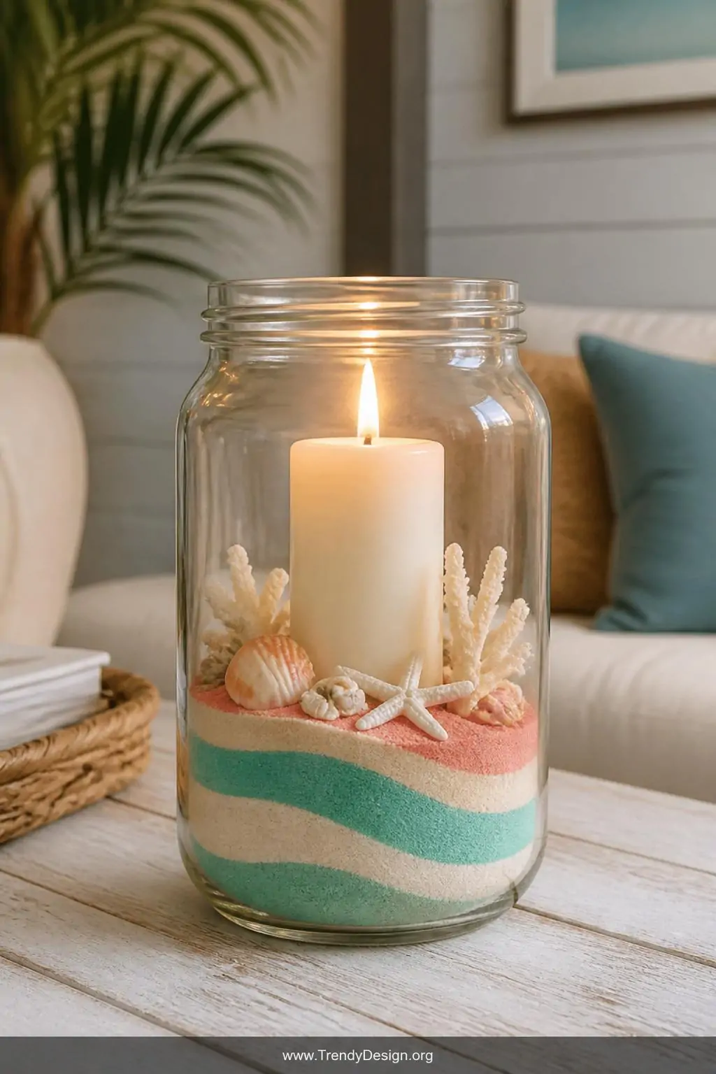 Mason jar filled with aqua, coral, and ivory layered craft sand surrounding a centered ivory pillar candle on a whitewashed wood coffee table, warm candlelight glow, coastal boho style, closeup