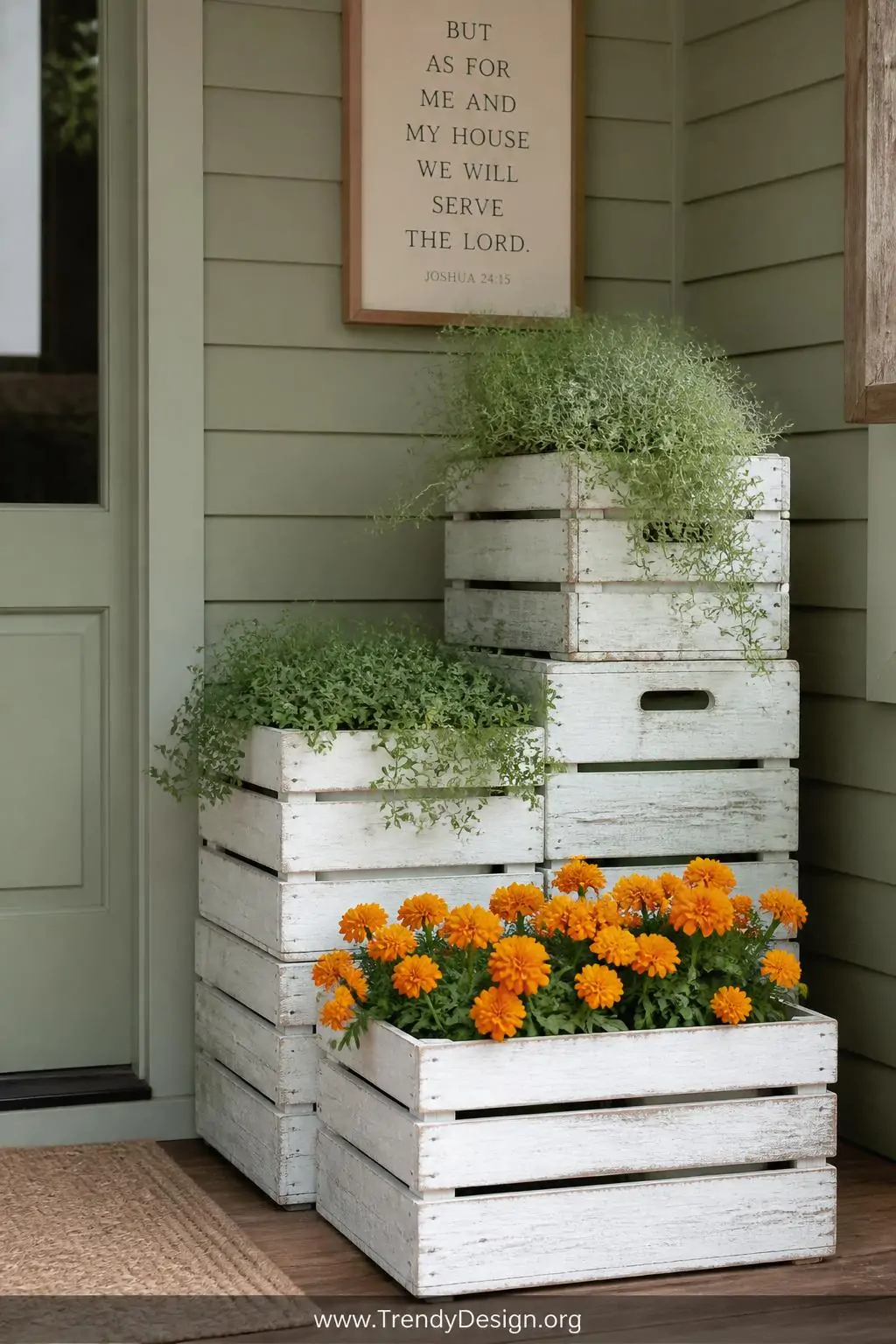 Stacked chalk-white wooden crates arranged at three tiered heights against a shiplap farmhouse porch wall, medium shot, planted with sage-green trailing herbs on top and vivid orange marigolds in the lower crate, rough-hewn wood texture contrasted against a soft muted sage painted surface, diffused natural daylight, photorealistic rustic farmhouse porch design.