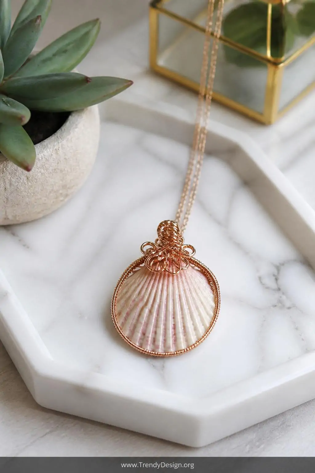 Wire-wrapped scallop shell pendant with gleaming gold copper wire coils hanging from a delicate chain displayed on a white marble jewelry tray beside a small succulent, bright natural boutique lighting, closeup shot, photorealistic interior design