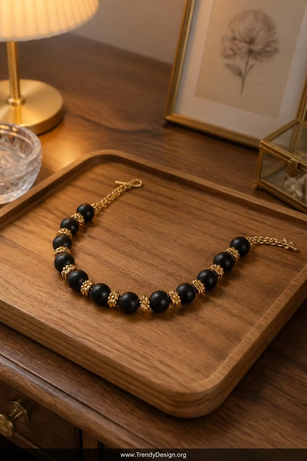 Mixed matte black round beads alternating with gold daisy spacer beads arranged in a graceful curve on a warm-toned oak vanity tray, boutique jewelry display styling, medium shot with soft warm lamp glow catching the metallic spacers against the dark matte texture.