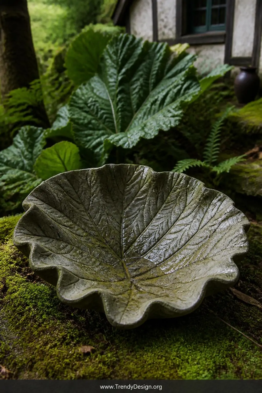 Leaf-cast concrete bird bath basin with deeply impressed rhubarb leaf veins and intricate natural textures, woodland garden setting, fairytale cottage style, earthy green and brown stained concrete surface revealing every delicate botanical detail, soft diffused natural daylight, resting on mossy ground, closeup shot capturing the stunning leaf impression.