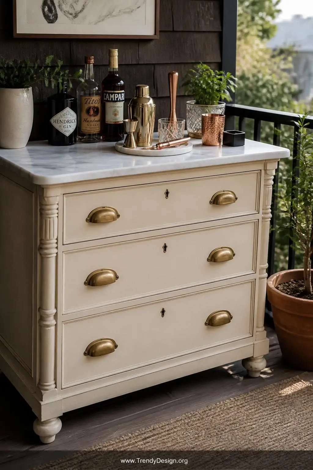 Medium shot of a vintage cream-painted dresser repurposed as an outdoor balcony bar station, topped with white marble-look vi