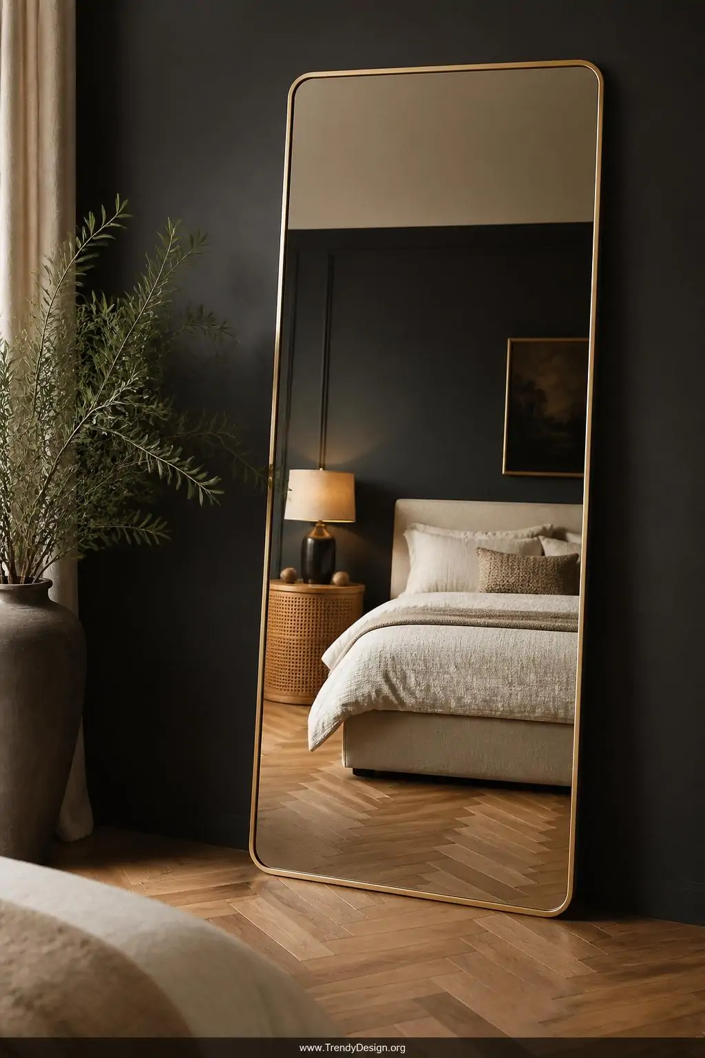Medium shot of a moody, luxurious bedroom corner where an oversized floor-to-ceiling leaner mirror with a slim warm brass fra