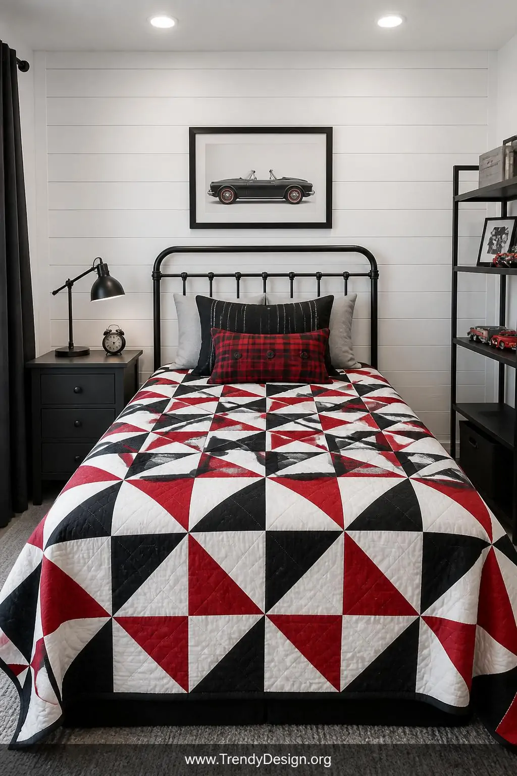 A pinwheel pattern quilt laid flat on a twin bed with white shiplap walls behind it, bold black and red geometric spinning sh