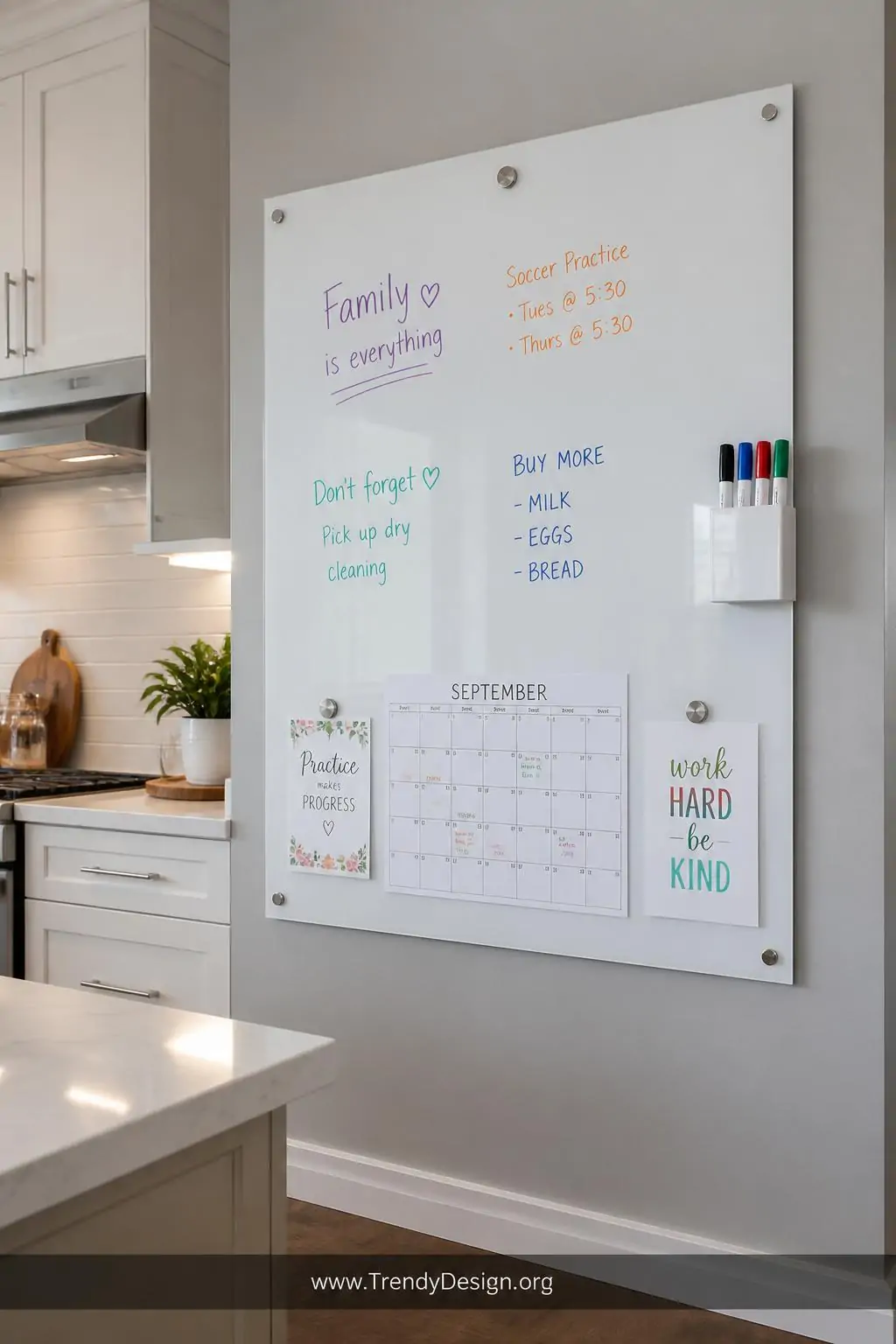 Large glossy white magnetic whiteboard panel mounted on a soft gray kitchen wall with colorful dry-erase notes, small magnetic cup holding markers clipped to the side edge, school calendar and appointment cards attached with silver round magnets, medium shot capturing the full board in a bright modern kitchen with under-cabinet lighting.