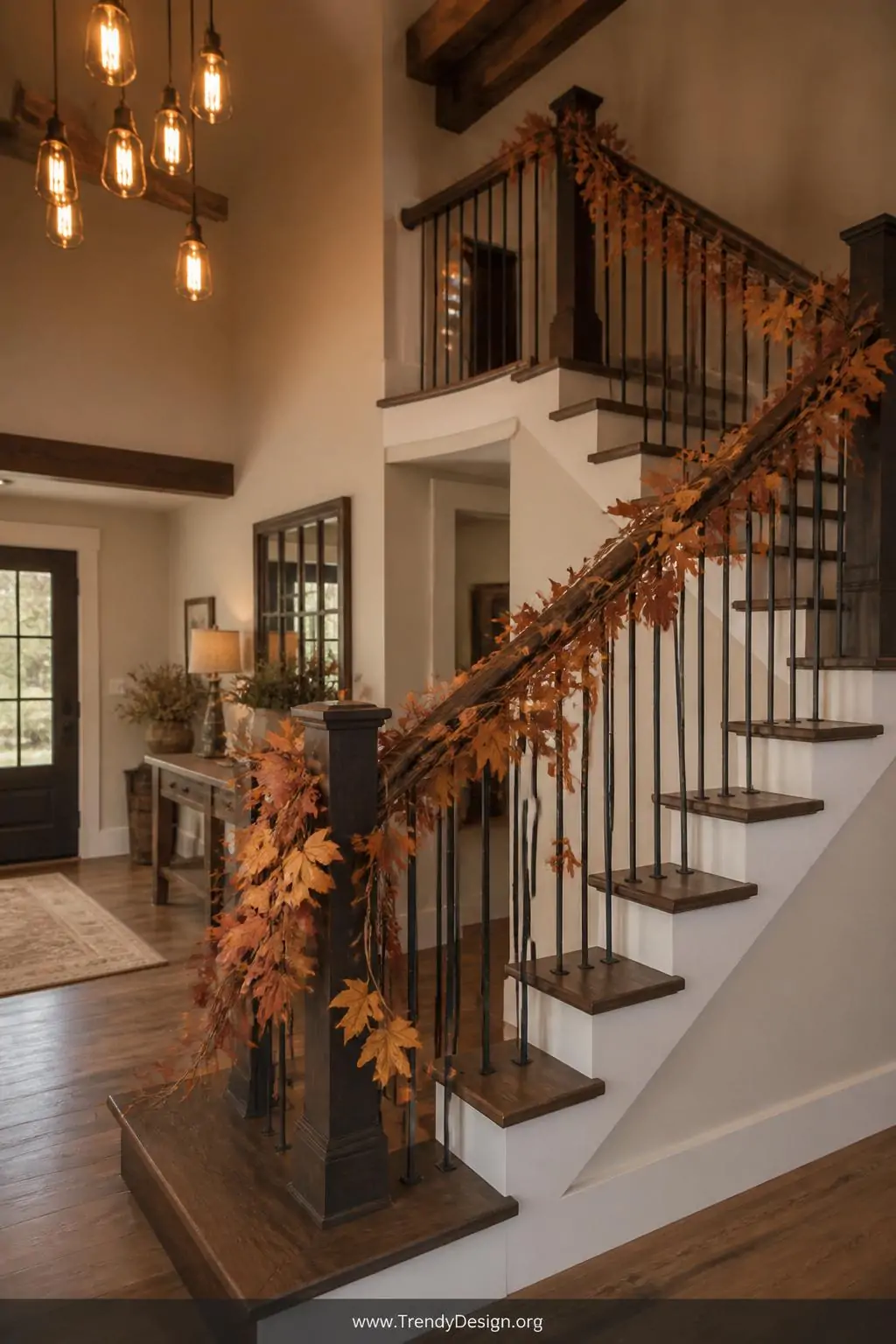 Rustic twine leaf garland wound along a dark wood staircase railing with dried amber and rust-colored leaves layered in varying sizes, soft warm Edison bulb lighting glowing from above in a farmhouse-style entryway, wide shot capturing the full staircase sweep.