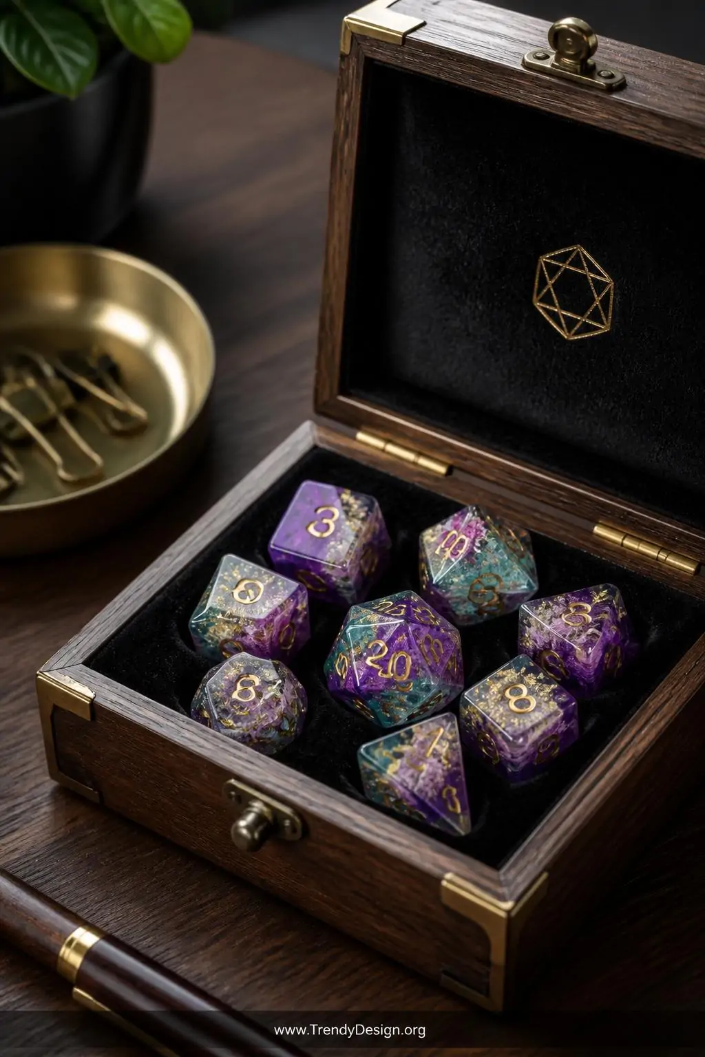 Resin polyhedral dice set with swirling purple and teal inclusions of dried flowers and gold foil flakes displayed in an open velvet-lined wooden box on a dark walnut desk, soft directional light catching translucent facets, closeup
