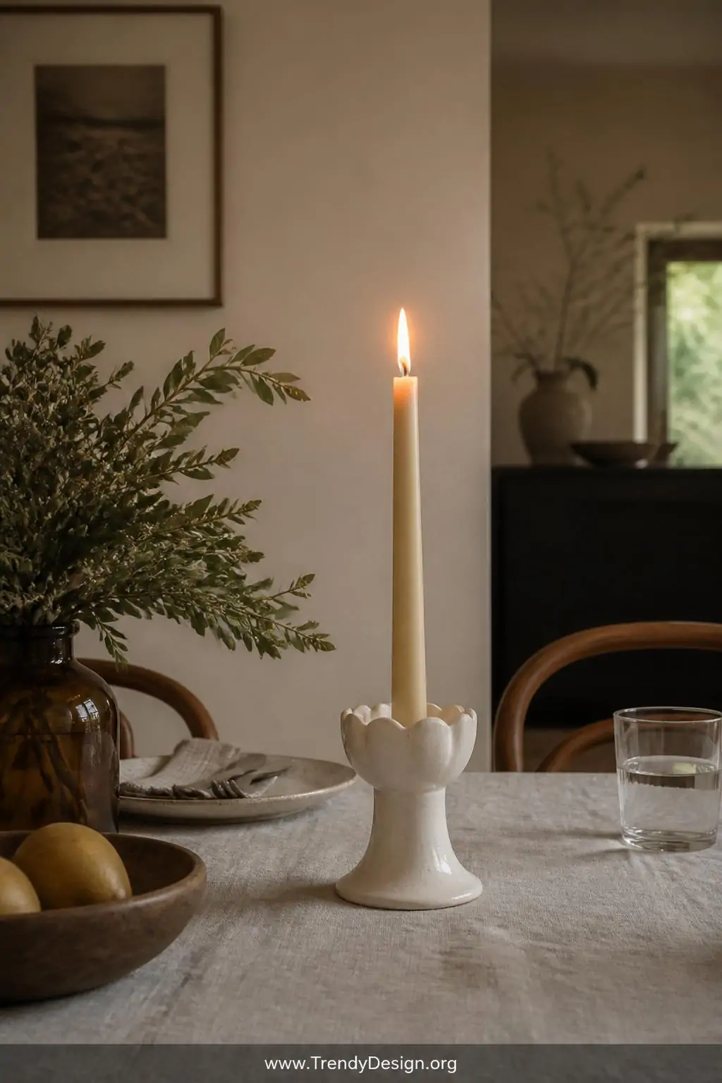 Matte white clay candle holder with hand-pinched scallop rim details glowing with a lit taper candle on a linen-draped dining table, soft golden candlelight, medium shot