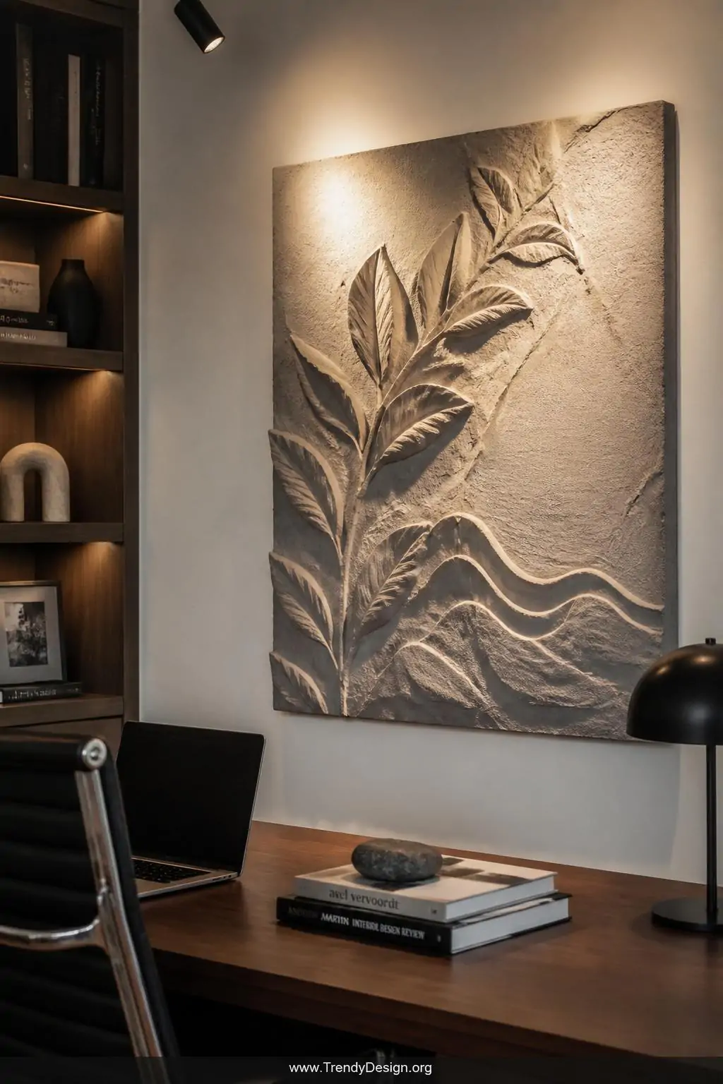 Fiber-reinforced concrete relief sculpture with raised botanical leaf and wave forms mounted on a backing board in a home office, warm directional spotlight emphasizing the three-dimensional depth and rough tactile texture against a clean white wall, medium shot, photorealistic interior design, no people.