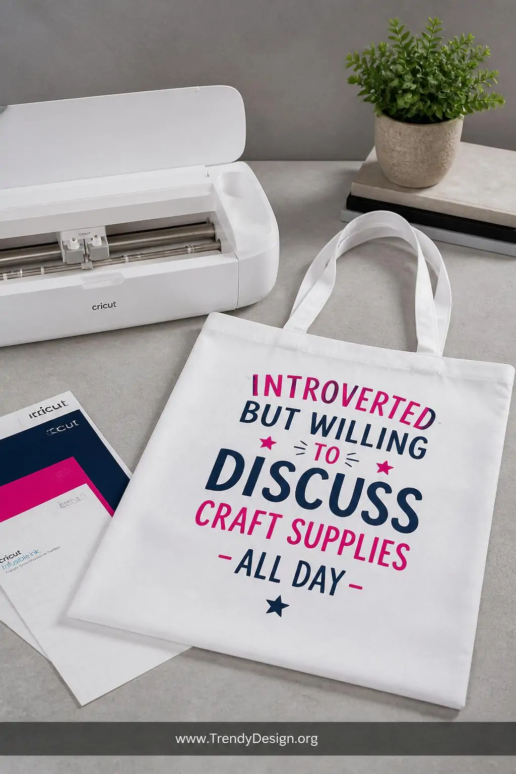 Crisp white polyester-blend tote bag with vibrant fuchsia and navy Infusible Ink funny quote lettering displayed flat on a light gray concrete countertop, cool studio lighting casting subtle shadows, wide shot showing the bag beside an open Cricut machine and ink transfer sheets.