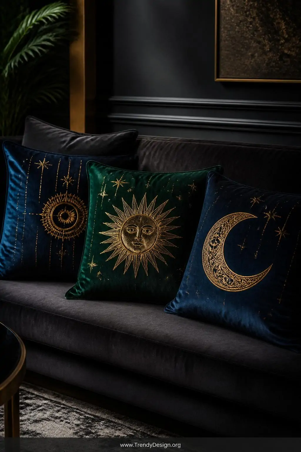 Deep jewel-toned velvet throw pillows with gold block-printed sun and moon celestial designs arranged on a charcoal velvet sofa, moody ambient lighting, the metallic stamped designs appearing almost three-dimensional against the rich emerald and sapphire velvet, medium shot