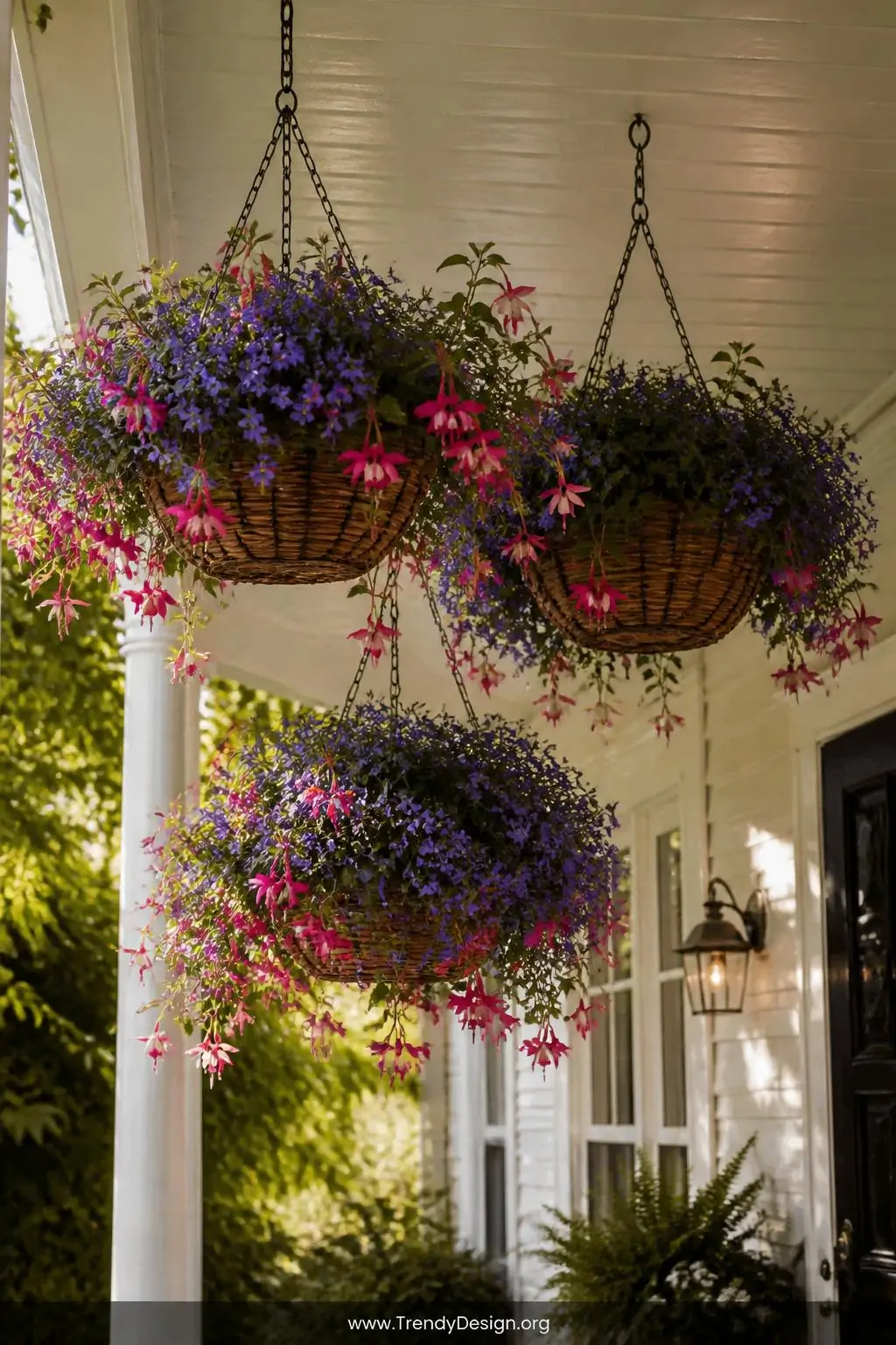 Three hanging wicker basket planters suspended at varying heights from a painted porch ceiling, medium shot, overflowing with cascading purple lobelia and hot pink fuchsia spilling dramatically over woven edges, warm dappled sunlight filtering through nearby foliage casting soft shadows, photorealistic cottage garden entryway design.