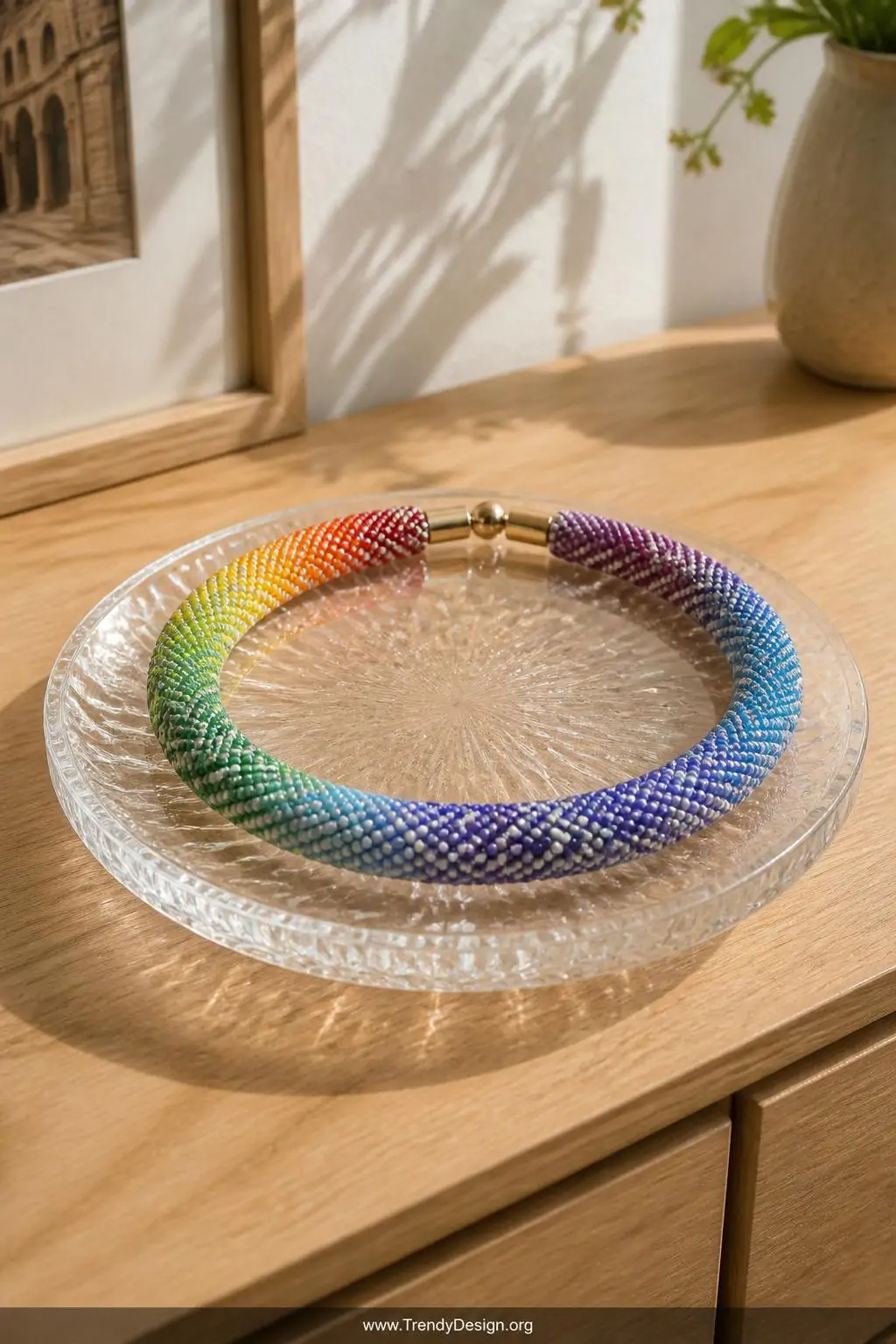 Rainbow gradient seed bead choker coiled on a glass display dish atop a light oak dresser, bright daylight illuminating the tiny bead surfaces, closeup revealing vivid multicolor stripes and intricate geometric pattern detail