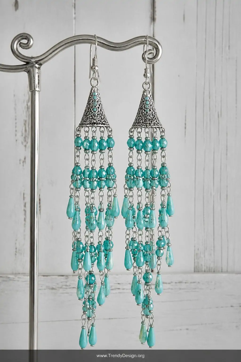 Tiered turquoise chandelier earrings with cascading bead strands hanging from a silver jewelry hook display against a weathered white shiplap wall, cool diffused natural light, closeup capturing the movement and drama of multiple delicate strands catching the light.
