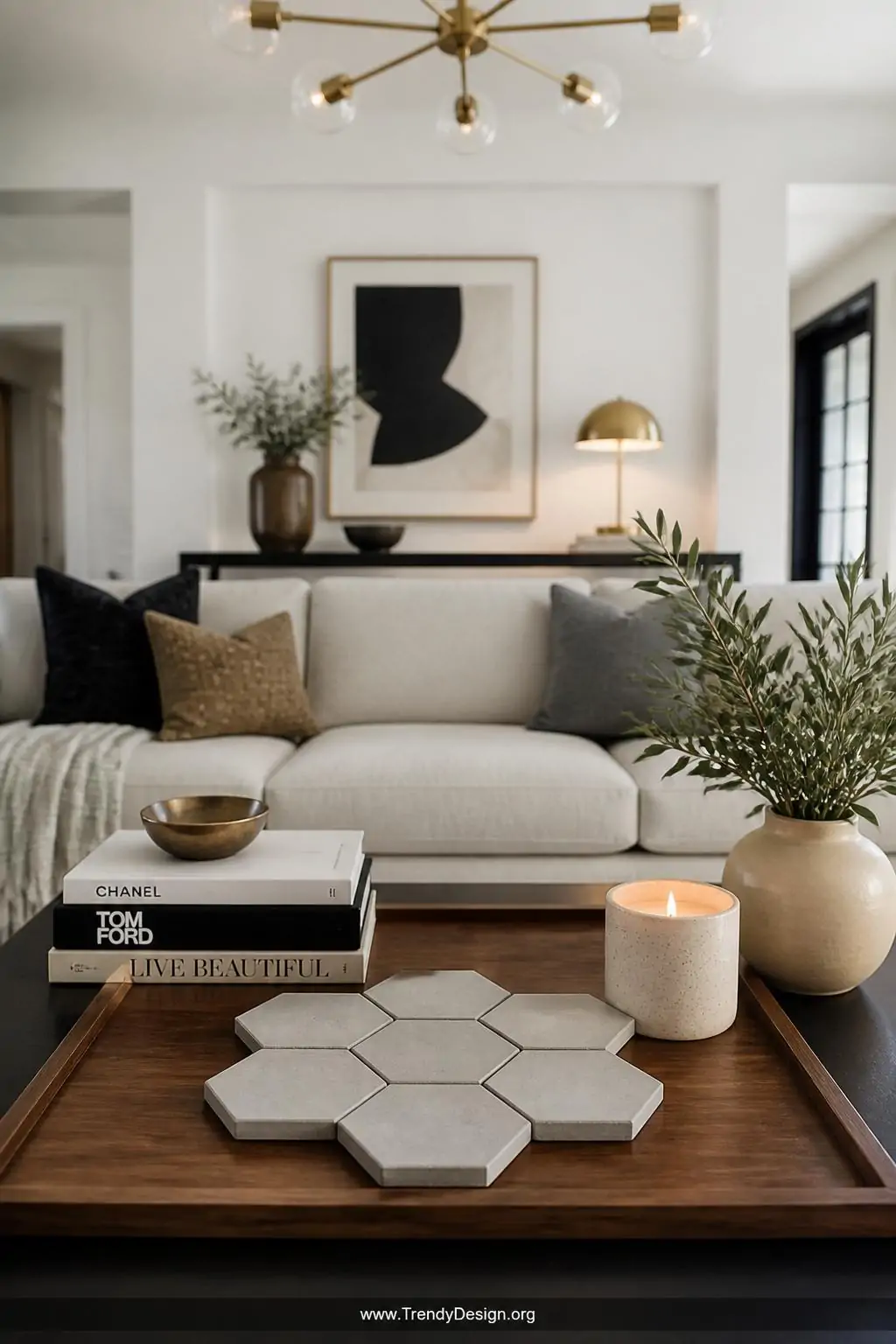 Hexagonal concrete coasters arranged in a honeycomb cluster on a warm walnut wood tray, contemporary living room with white walls and brass accent lighting overhead, wide shot showing the full coffee table vignette with styled books and a ceramic candle alongside.