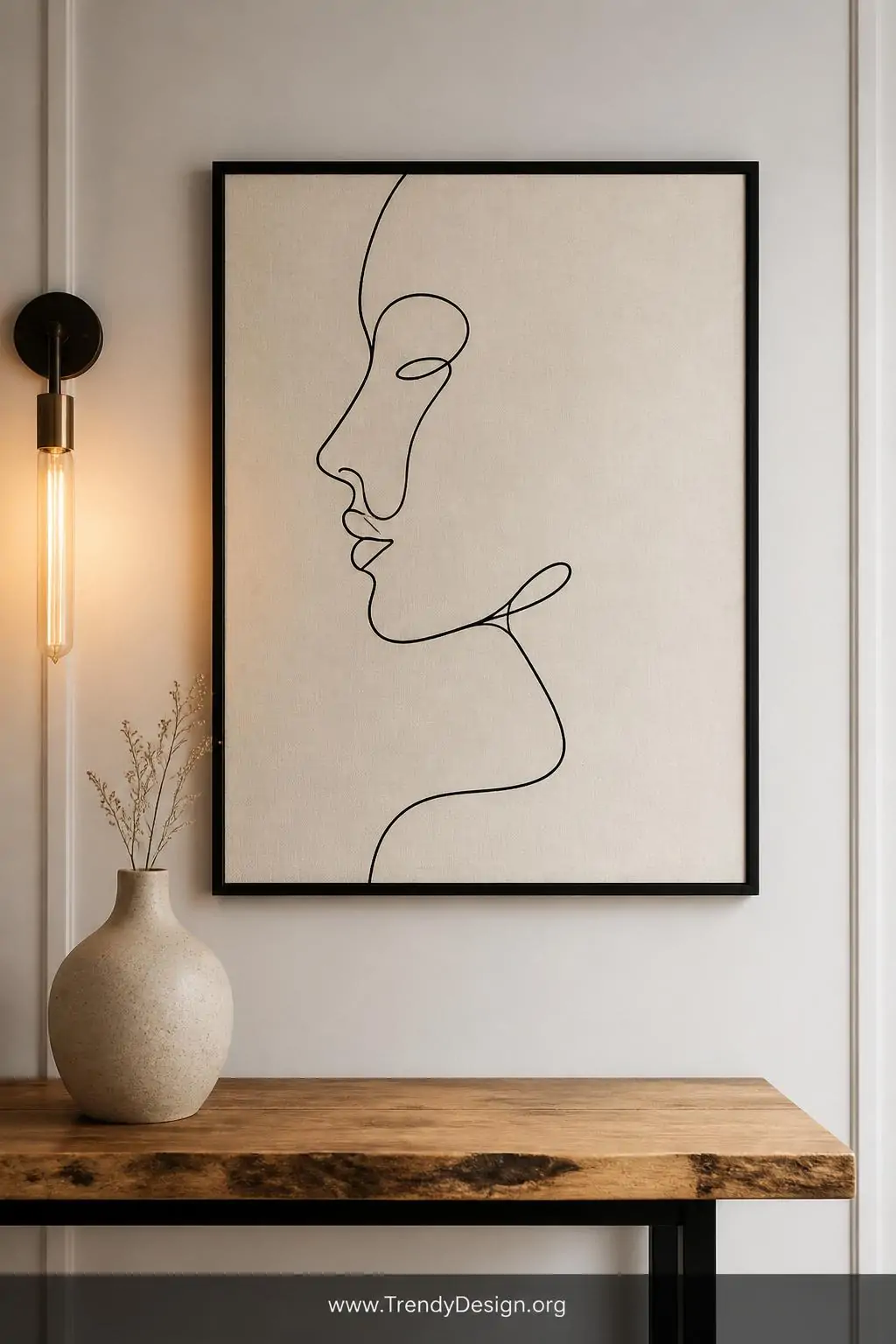 Closeup shot of a single framed minimalist line art canvas mounted on a soft white wall above a slim natural wood console tab