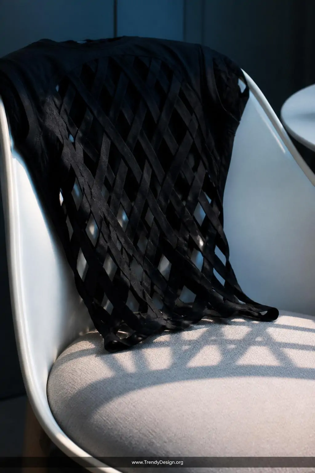 A closeup of a stretched lattice-cut black jersey t-shirt draped dramatically over the back of a sleek white mid-century mode