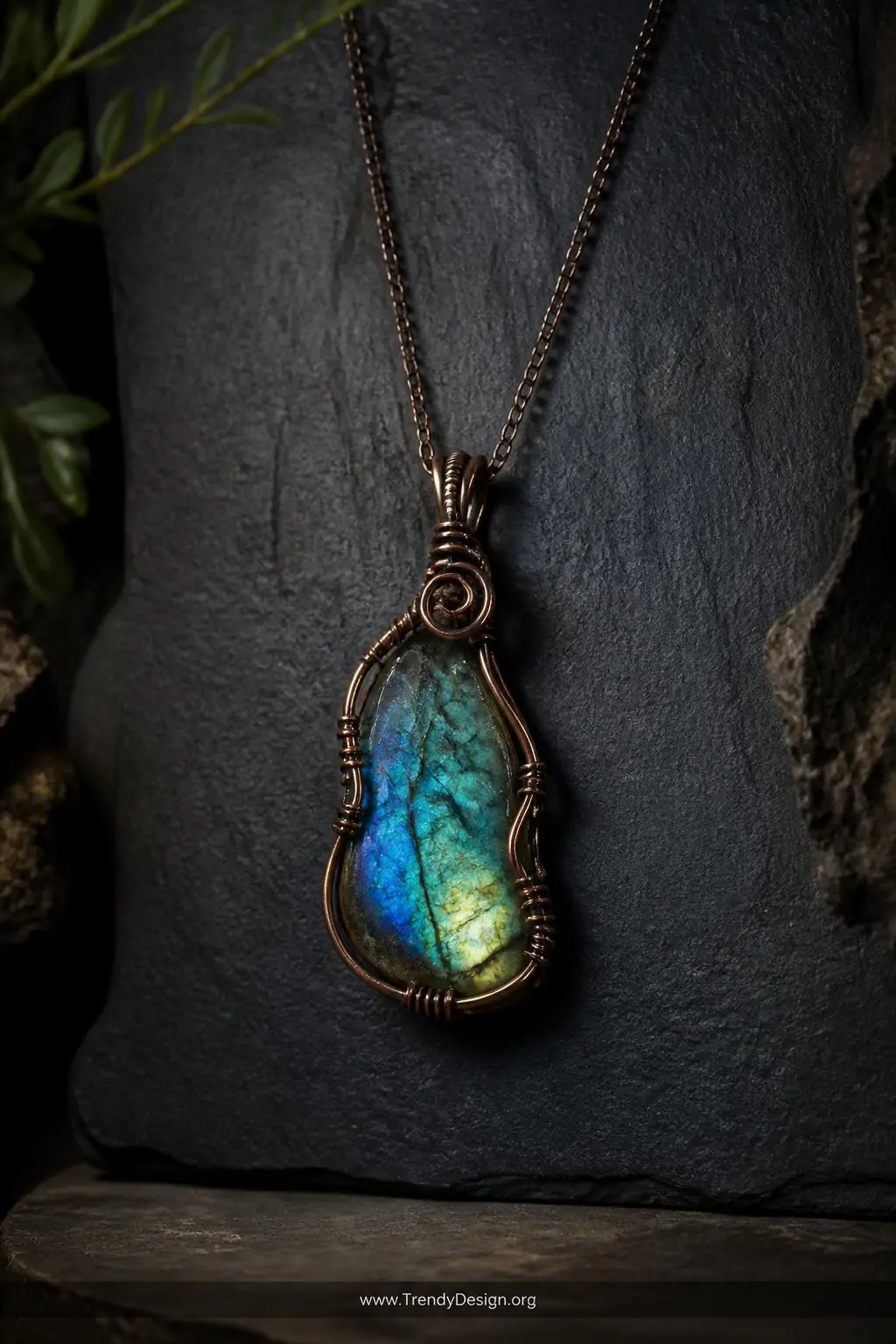 Freeform labradorite slice pendant in oxidized copper wire displayed on a dark slate jewelry board, moody directional side lighting revealing iridescent blue-green flash within the stone, medium shot showing organic wire placement along stone edges