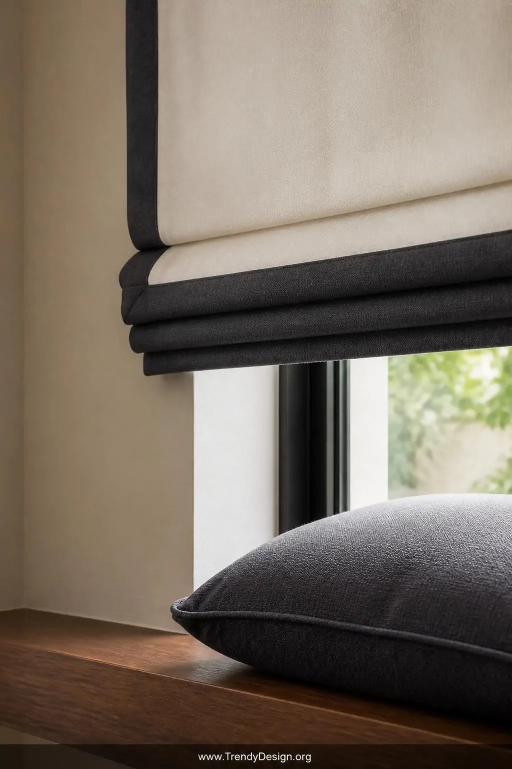 A detailed close-up of a raised ivory Roman blind with a wide deep-charcoal contrast border band along the bottom hem, the da